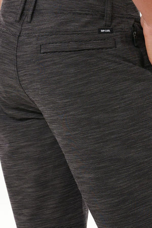 A close-up view highlights someone wearing dark gray, textured Rip Curl Jackson Boardwalk pants. These pants feature a back pocket with a tiny "Rip Curl" label above it and are crafted from quick-dry, water-repellent fabric, combining style with practicality for any adventure.