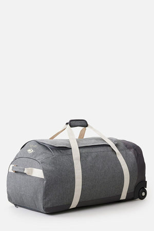 The Rip Curl Jupiter 80L Classic Surf Travel Bag is a spacious gray duffel with beige straps and wheels, ideal for surf travel. It includes a top handle and a zippered side pocket, all designed to be lightweight and eco-friendly.