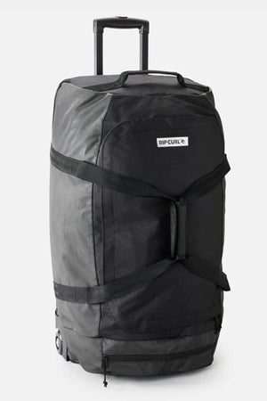 A large Rip Curl Jupiter 80L Icons Travel Bag in black, featuring wheels and a retractable handle for easy transportation. The bag includes sturdy black straps, a shoe pocket, and a front label. This design emphasizes utility and durability, making it perfect for travel or heavy-duty use.