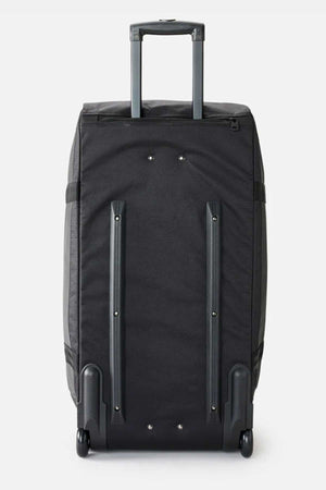 The Rip Curl Jupiter 80L Icons Travel Bag, shown from the back, is a black wheeled travel suitcase made from recycled polyester. It features a retractable handle, two sturdy supporting bars, and small wheels at the bottom for easy maneuverability. This durable bag is ideal for travel and includes a convenient shoe pocket.