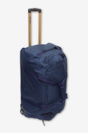 The Rip Curl Jupiter 80L Mixed Travel Bag is a blue rolling duffel featuring a retractable top handle, black wheels, and lightweight construction with multiple handles and straps for versatile carrying options. Made from recycled polyester, this durable bag has a textured surface displaying the brand name near the top.