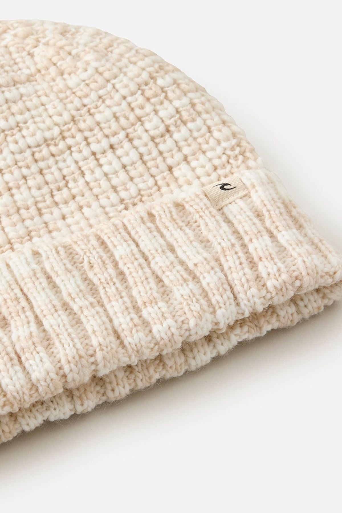 Close-up of the Rip Curl Keep Sakes Reg Beanie, a cream-colored ribbed knit with a small "c" fabric tag on the cuff, ideal for coastal adventures. The beanie is displayed against a white background.