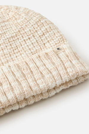 Close-up of the Rip Curl Keep Sakes Reg Beanie, a cream-colored ribbed knit with a small "c" fabric tag on the cuff, ideal for coastal adventures. The beanie is displayed against a white background.