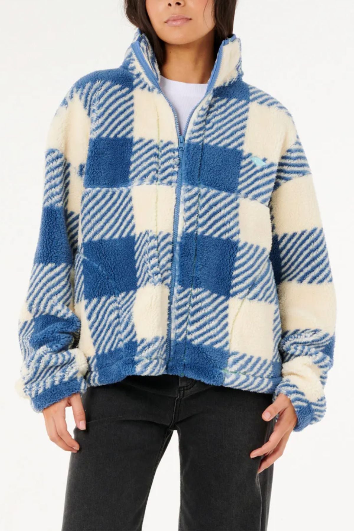 A person wears the Rip Curl Neon Isles Zip Through Polar Fleece—a fluffy blue and white checkered recycled polyester jacket—over a white top and black jeans, standing against a plain white background with their face partially visible.