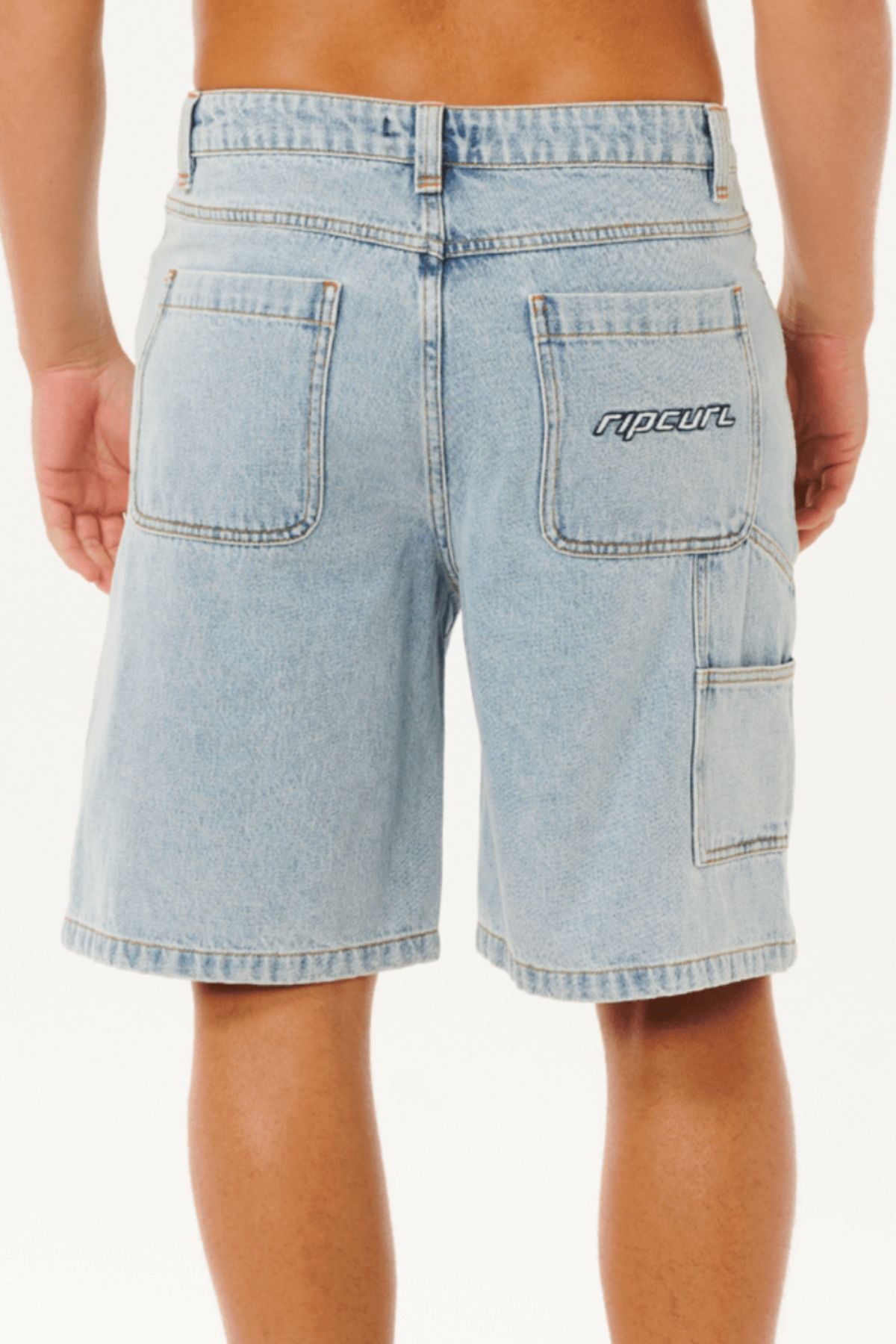 A person is seen from behind wearing Rip Curl Nu Dose Denim Walkshorts in light blue, featuring a baggy fit, oversized carpenter pockets, and "ripcurl" embroidery on the right pocket, all set against a plain white background.
