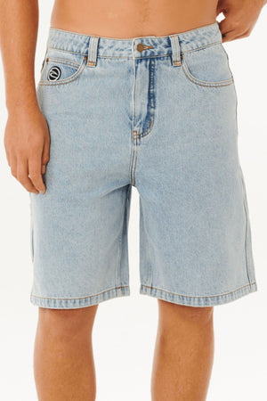 A person wears Rip Curl Nu Dose Denim Walkshorts in light blue, shown from waist to mid-thigh, featuring a button and zip closure, front and carpenter pockets, and a small black and white logo on the left pocket against a white background.