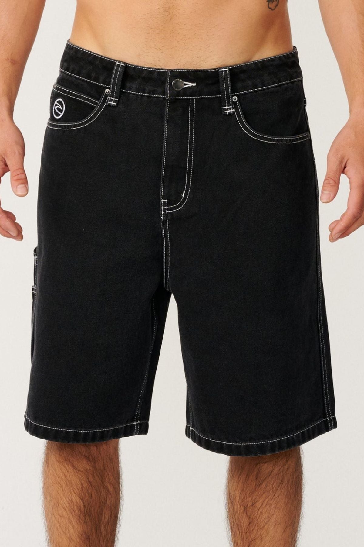 A person wearing the Rip Curl Nu Dose Denim Walkshort in black—with white stitching, side and front pockets, and a button closure—stands against a plain background with their torso bare.