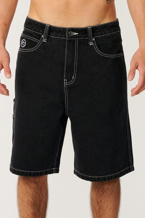 A person wearing the Rip Curl Nu Dose Denim Walkshort in black—with white stitching, side and front pockets, and a button closure—stands against a plain background with their torso bare.