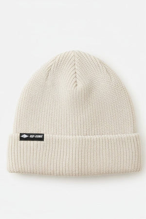The Rip Curl Oceanic Reg Beanie is a light beige knit with a folded brim and a small black patch showing white text and the Rip Curl logo—ideal for staying warm after water sports.