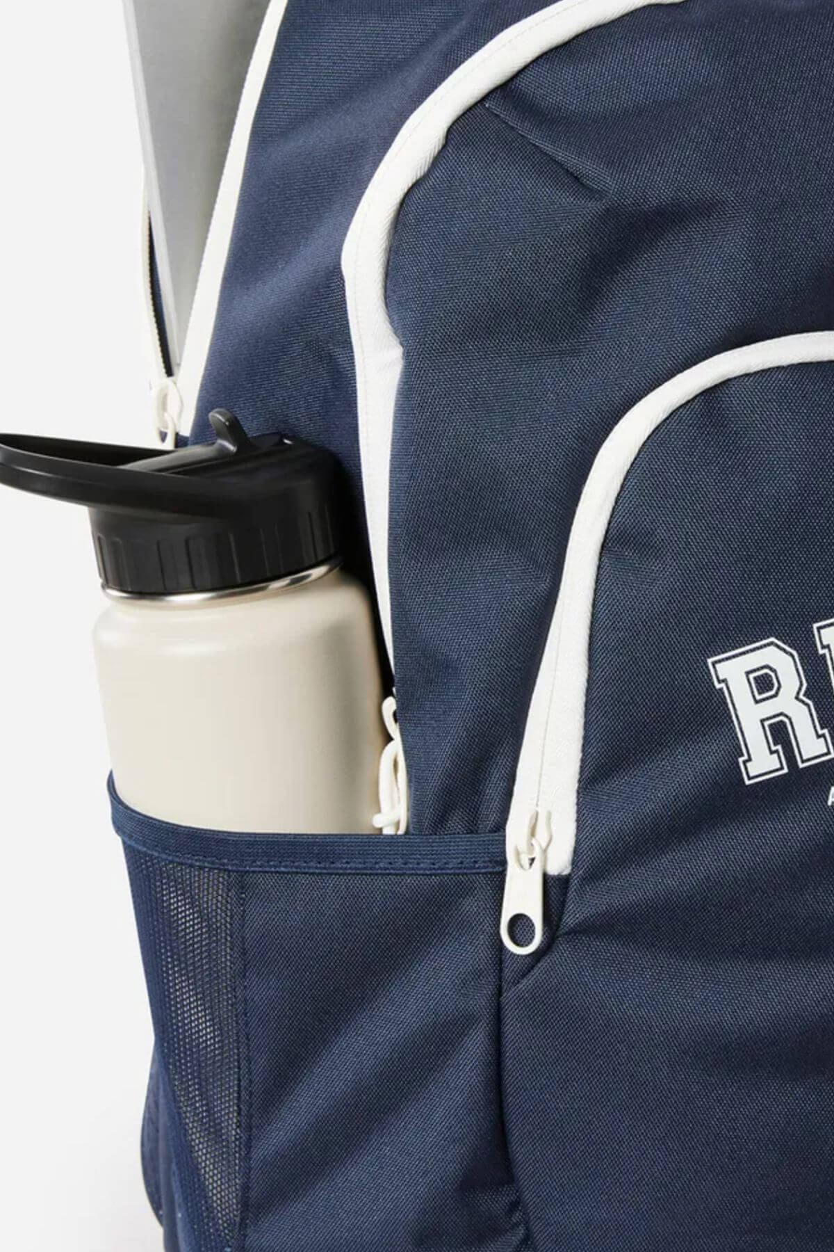 A close-up of the Rip Curl Ozone 2.0 30L Backpack with white zippers and trim, showcasing a beige water bottle in a side mesh pocket and part of the word "REP" visible on the bag.