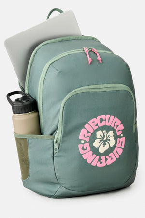 A green Rip Curl Ozone 2.0 30L Backpack with a pink logo and floral design, shown with a silver laptop in the main compartment and a beige water bottle in the side pocket, set against a plain light background.