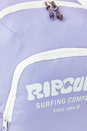 Close-up of a Rip Curl Ozone 2.0 30L Backpack in light purple, featuring white zippers and accents. The text on the pocket reads "RIP CURL SURFING COMPANY SINCE 1969" in white letters, highlighting its durable polyester construction.