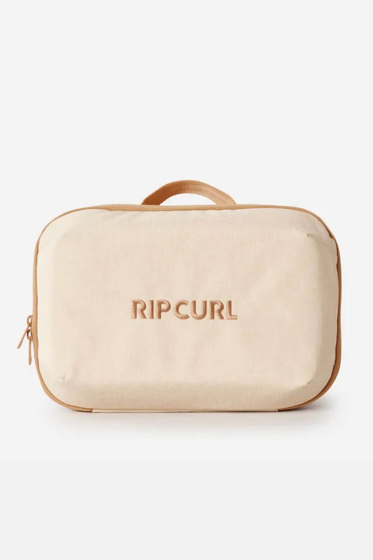 The Rip Curl Ultimate Beauty Case is a rectangular beige beauty case made from recycled polyester, featuring a zipper, small top handle, internal mesh organiser, and "RIP CURL" embroidered on the front.