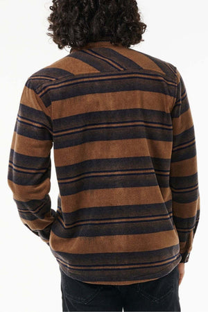 A person with curly hair is shown from the back wearing a Rip Curl Party Pack Polar Fleece Shirt made from recycled polyester. The long-sleeve, brown and black striped shirt is perfect for cooler weather. The individual stands against a plain white background.