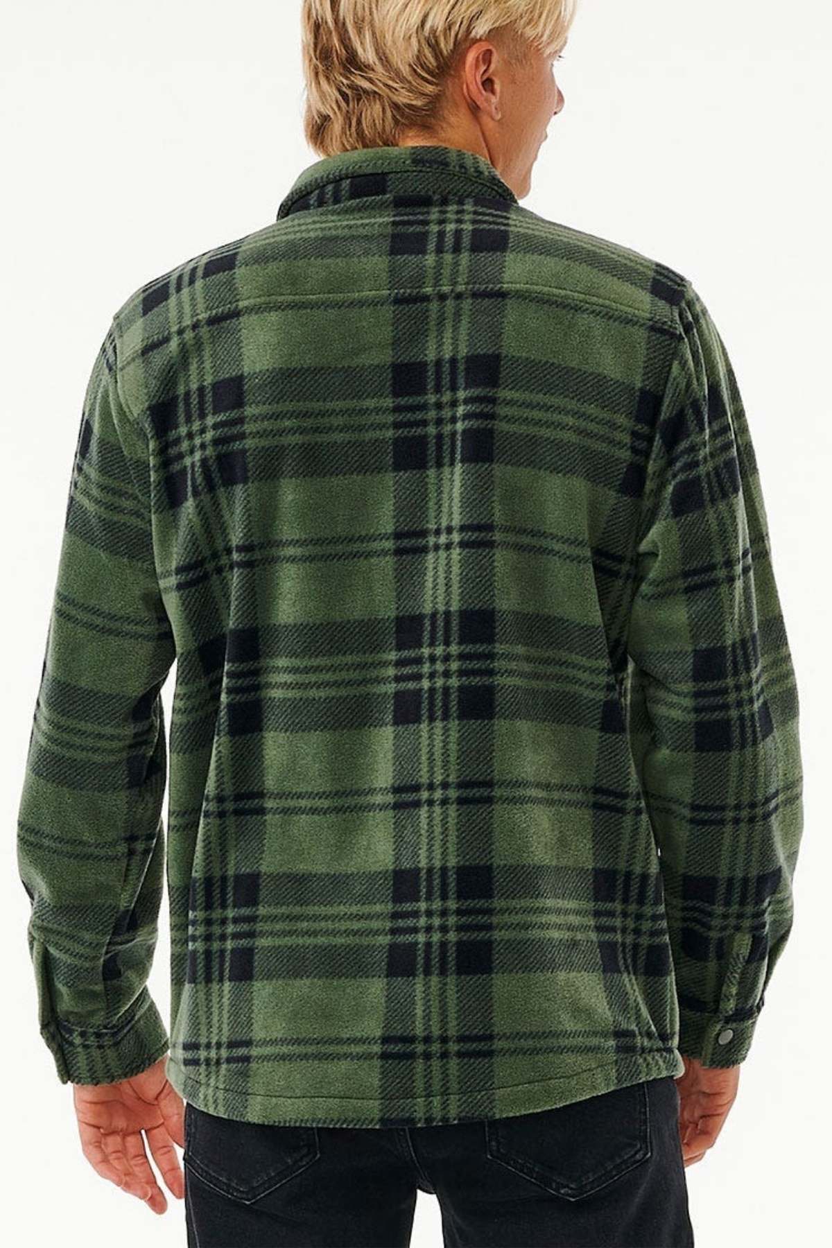 A person with blonde hair, standing and facing away from the camera, is wearing a green and black plaid Rip Curl Party Pack Polar Fleece Shirt crafted from recycled polyester along with black pants. The backdrop is plain white.