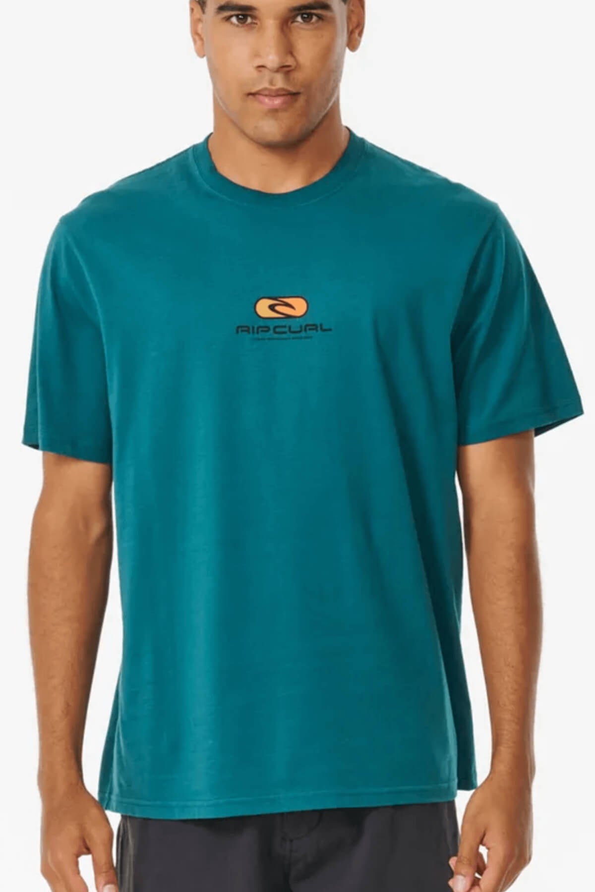 Against a white background, someone wears a teal Rip Curl Pill Icon Tee, featuring a small logo and text on the front. Made from 100% cotton.