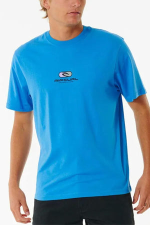 A man in a bright blue Rip Curl Pill Icon Tee, made of cotton, with a black "AIRCUAL" logo on the chest, pairs it with dark pants. The relaxed fit stands out against the plain white background.