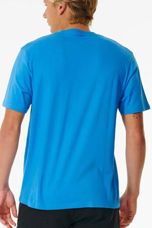 With light brown hair, they wear a bright blue short-sleeved Rip Curl Pill Icon Tee made of soft cotton. They're turned away, showing a tattoo on their left forearm. The T-shirt has a relaxed fit against a plain white backdrop.