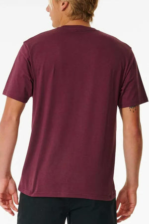 A blonde-haired person is seen from behind wearing the maroon Rip Curl Pill Icon Tee (100% cotton) with black pants, standing against a plain white background.