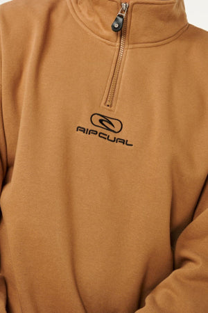 A person wearing a brown Rip Curl Pill Icon 1/4 Zip Crew made from organic cotton fleece, featuring a small black zipper and an embroidered "AIRCUAL" logo on the chest. The person's head is not visible.