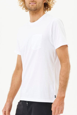 A person with curly hair is wearing a Rip Curl Plain Pocket Tee, crafted from 100% cotton. This standard fit T-shirt features a chest pocket and short sleeves, paired with black pants. They are positioned against a plain light background, although their face isn't fully visible.