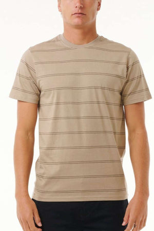 A person is standing against a plain white background, wearing the Rip Curl Plain Stripe Tee in beige, which features thin horizontal lines, short sleeves, and a crew neckline. The person is also wearing black pants, and their face is not fully visible.