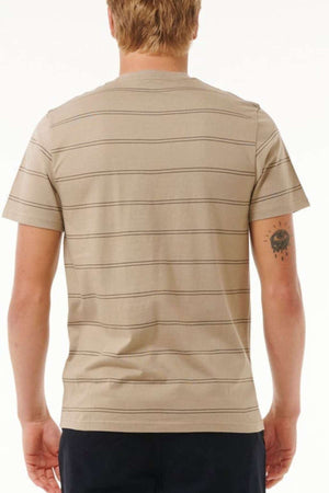 A person with light hair is wearing a beige cotton Rip Curl Plain Stripe Tee with thin horizontal stripes. They have a small tattoo on their left arm, featuring a smiling sun with raindrops below it. The individual is shown from behind.