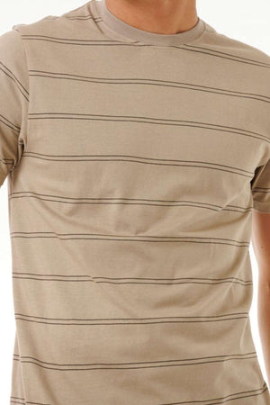 A person wearing a Rip Curl Plain Stripe Tee featuring thin horizontal black stripes on a beige cotton fabric. The focus is on the upper body, showcasing the shirt's pattern and fit against a plain white background.