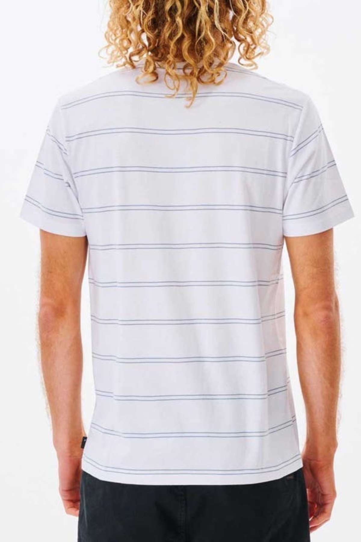 A person with curly blonde hair is dressed in a Rip Curl Plain Stripe Tee, crafted from 100% cotton to ensure maximum comfort. The short-sleeved t-shirt is white with thin horizontal gray stripes. They wear it with dark pants and are photographed from behind against a plain white backdrop.