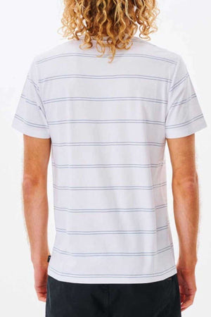 A person with curly blonde hair is dressed in a Rip Curl Plain Stripe Tee, crafted from 100% cotton to ensure maximum comfort. The short-sleeved t-shirt is white with thin horizontal gray stripes. They wear it with dark pants and are photographed from behind against a plain white backdrop.