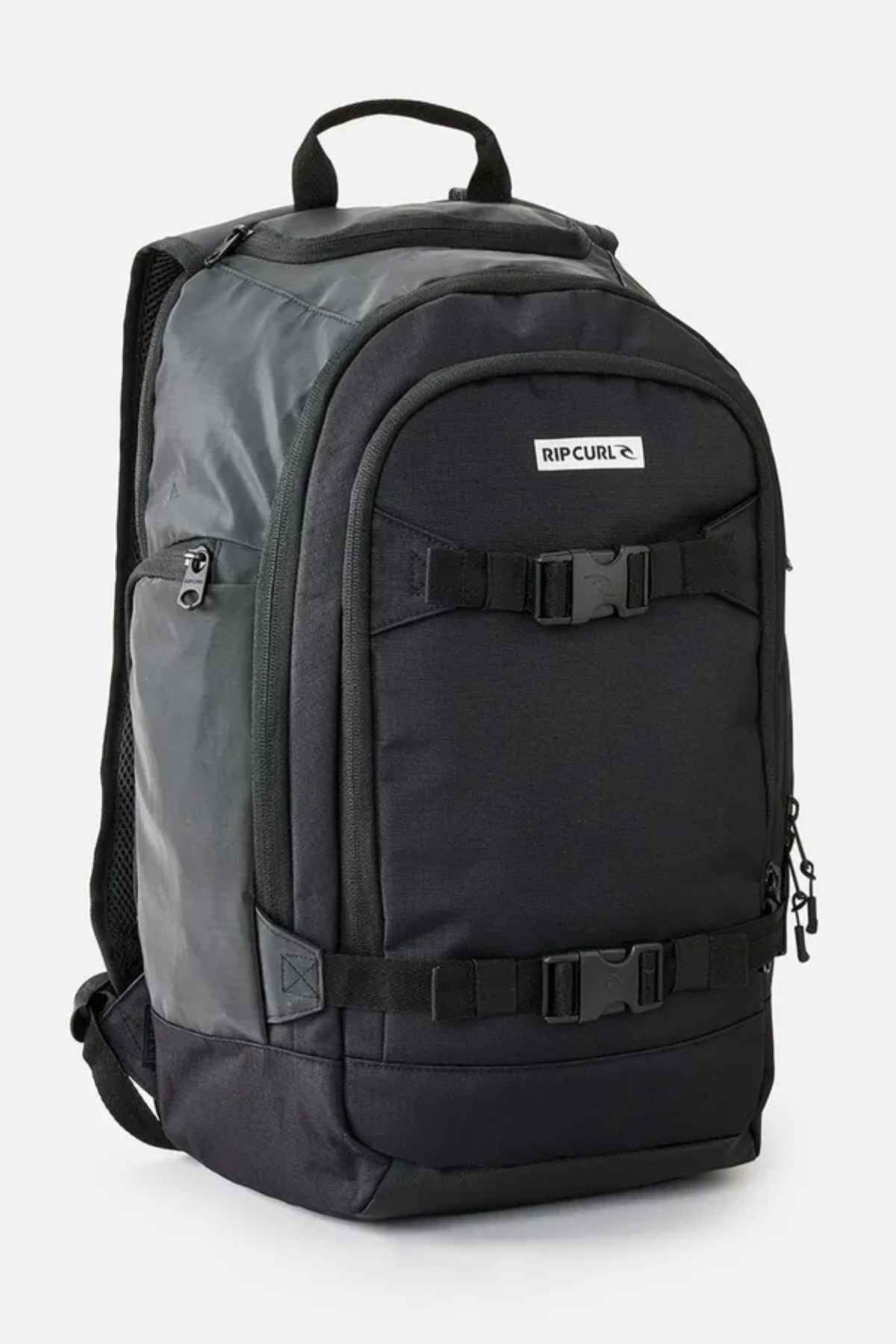 The black and dark green Rip Curl Posse 33L Icons Backpack showcases multiple compartments, including a laptop section, and comes with adjustable straps. Made from recycled polyester, it stands upright against a white background.