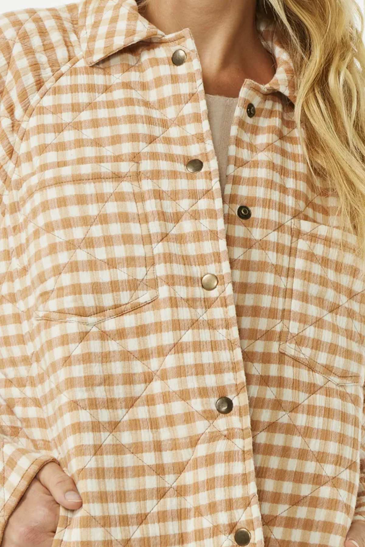 Close-up of a person wearing the Rip Curl Premium Quilted Check Jacket in beige and white, made from cotton double weave with metal snap buttons. It features two breast pockets, and their long, wavy blonde hair falls to the right.