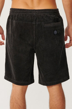 A person is seen from the back wearing Rip Curl Premium Surf Cord 19" Volley shorts in black, featuring an elastic waistband, a back pocket, and a patch above the pocket.