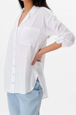 A woman models the Rip Curl Premium Surf Long Sleeve Button Up Shirt, featuring a chest pocket and rolled-up sleeves, paired with light blue jeans. She poses with a hand on her hip against a plain white background.