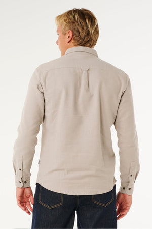 A man with short blonde hair is shown from the back, wearing a Rip Curl Premium Surf Flannel and dark blue jeans, standing against a plain white background.