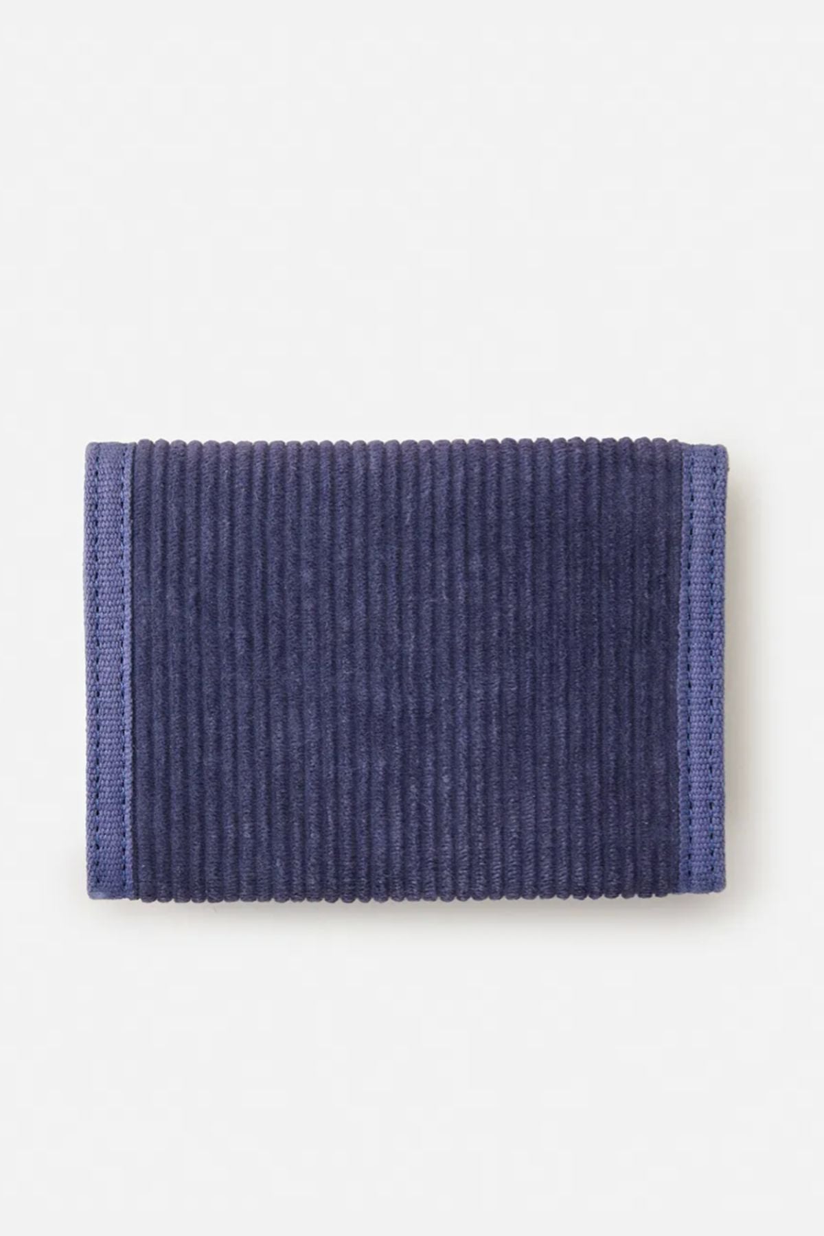 The Rip Curl Revival Cord Surf Wallet, rectangular and dark blue with a ribbed corduroy texture and stitched edges, lies flat on a light background.