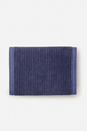 The Rip Curl Revival Cord Surf Wallet, rectangular and dark blue with a ribbed corduroy texture and stitched edges, lies flat on a light background.