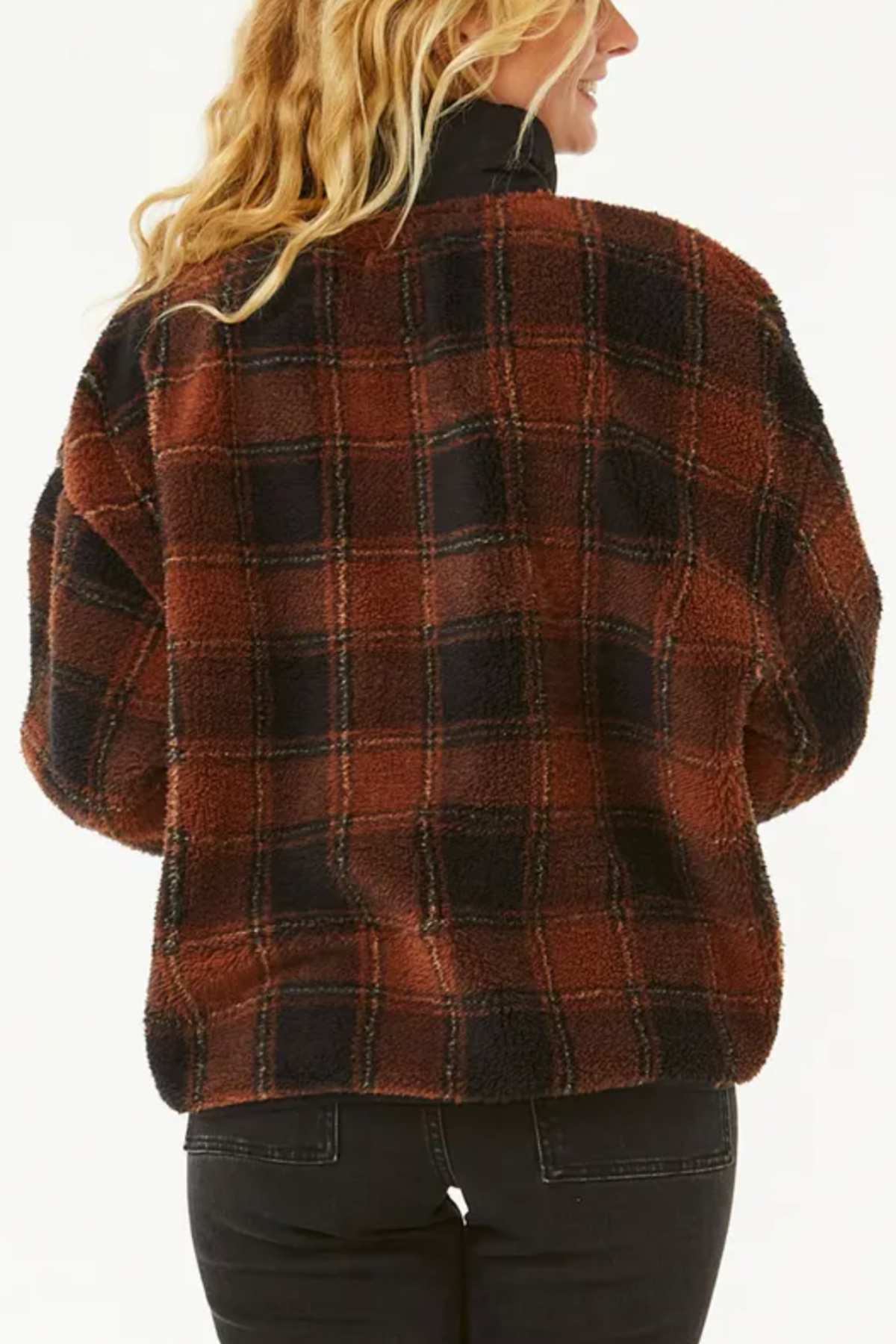 A person with long wavy blond hair is seen from behind, wearing the Rip Curl Sea Of Dreams Check Fleece in brown and black plaid with black jeans, set against a plain light background.