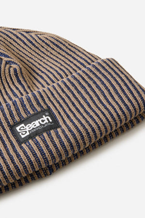 A close-up of the Rip Curl Search Chunky Reg Beanie, a ribbed knit winter hat with brown and navy stripes, featuring a black rectangular patch reading “Search.” This cozy cotton beanie is perfect for chilly days.