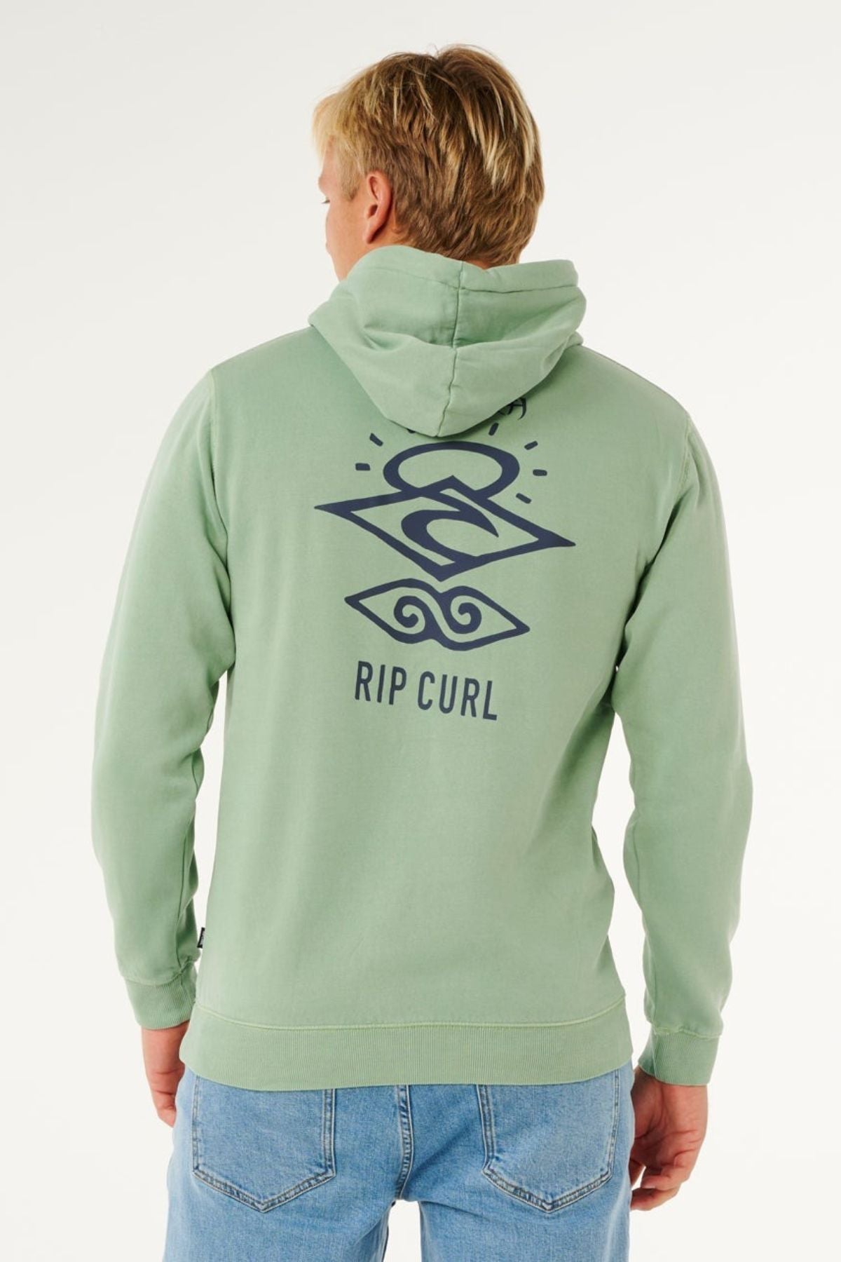 A blonde-haired person faces away from the camera, wearing the Rip Curl Search Icon Hood in light green with a dark blue abstract design and "RIP CURL" on the back, paired with light blue jeans.