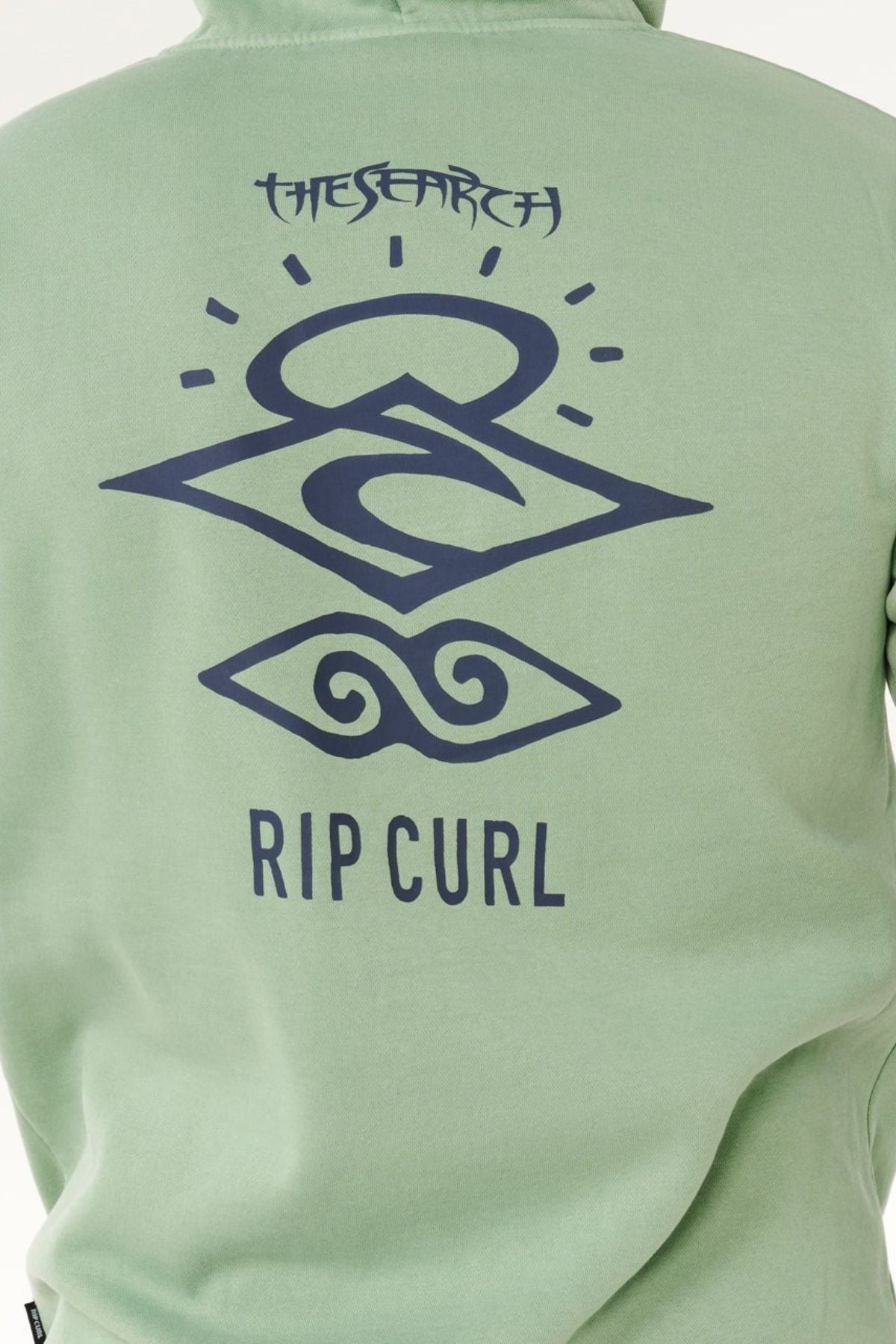 A green Rip Curl Search Icon Hood made from organic cotton, featuring dark blue geometric wave designs and “THE SEARCH” printed on the back.