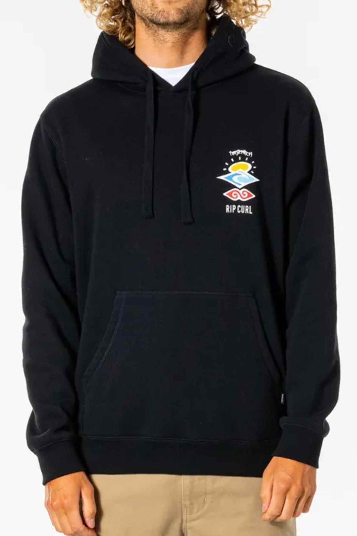 A person wears the Rip Curl Search Icon Hood in black—an organic cotton hoodie with a small colorful left chest graphic, front pocket, and drawstrings—paired with tan pants. Their face is partially out of frame.
