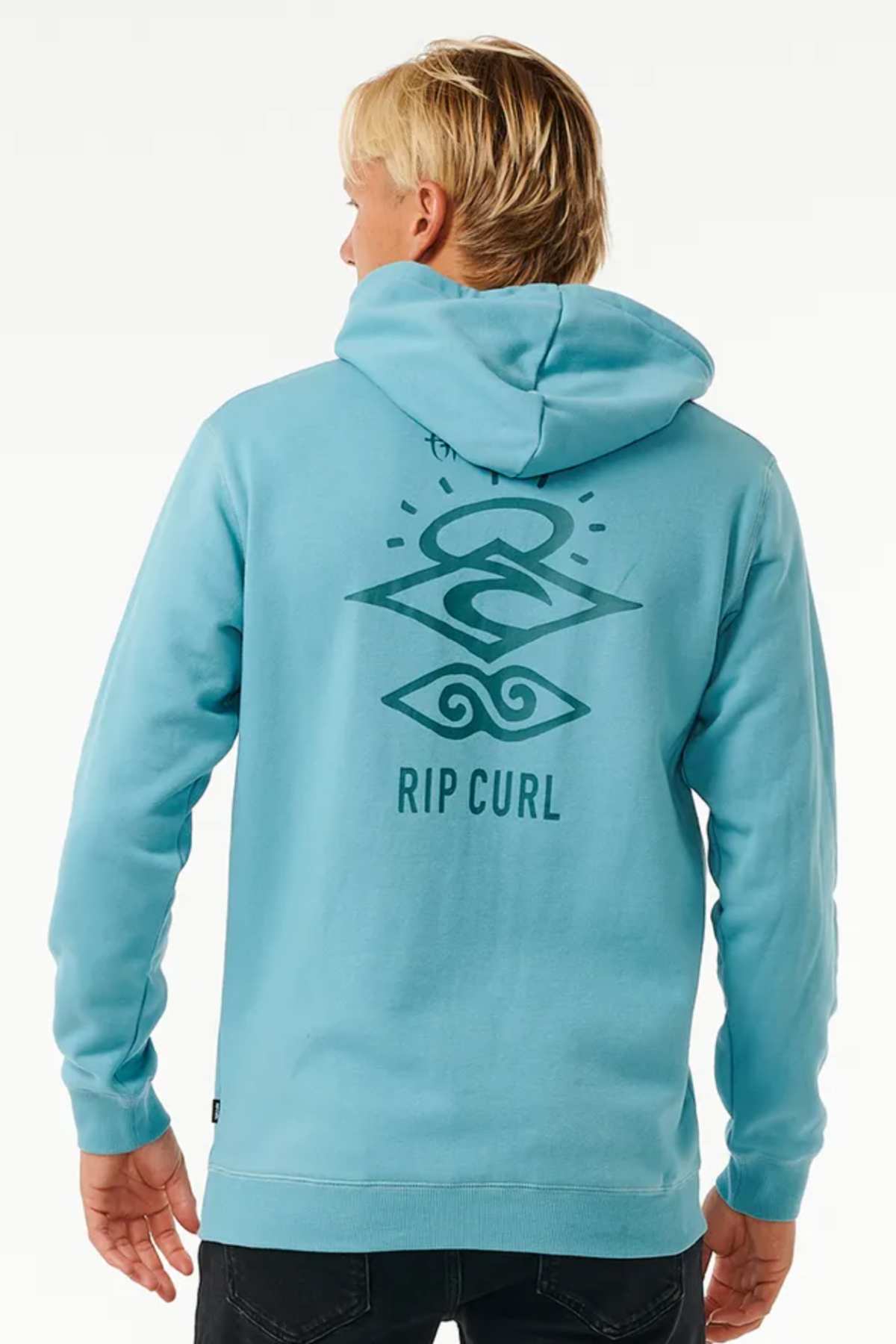 A person with light blonde hair is seen from behind, wearing a light blue Rip Curl Search Icon Hood. The hoodie, made of Organic Brushed Cotton and featuring a cozy fleece lining, has a large graphic design on the back with abstract shapes and the text "RIP CURL." The background is plain and light.
