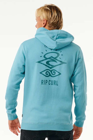 A person with light blonde hair is seen from behind, wearing a light blue Rip Curl Search Icon Hood. The hoodie, made of Organic Brushed Cotton and featuring a cozy fleece lining, has a large graphic design on the back with abstract shapes and the text "RIP CURL." The background is plain and light.