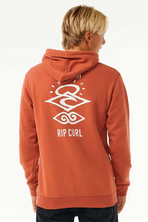 A person with blonde hair is seen from the back wearing a terracotta Rip Curl Search Icon Hood made from organic cotton, featuring a white geometric logo and "RIP CURL" lettering on the back.
