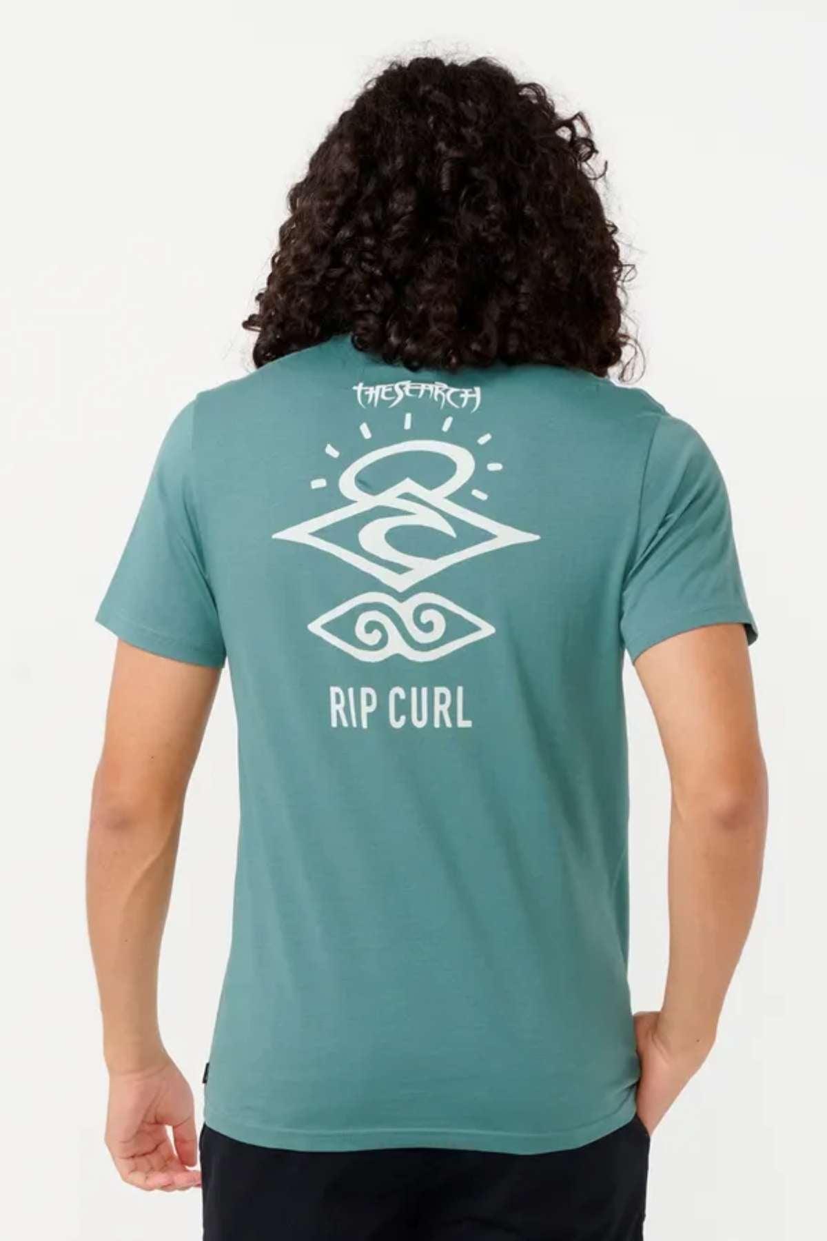 A person with long curly hair is sporting a teal "Rip Curl Search Icon Tee" in lightweight cotton, featuring a white abstract design on the back, perfect for outdoor activities.