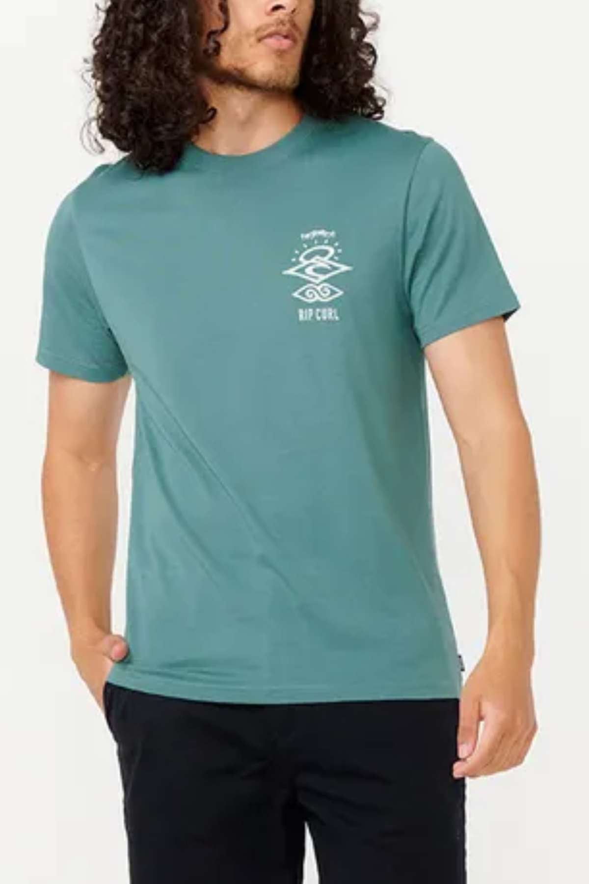 A person with long curly hair is wearing a teal Rip Curl Search Icon Tee made from lightweight cotton, featuring a small white graphic on the left chest. They are also wearing black pants, standing against a plain backdrop, ready for an outdoor activity.