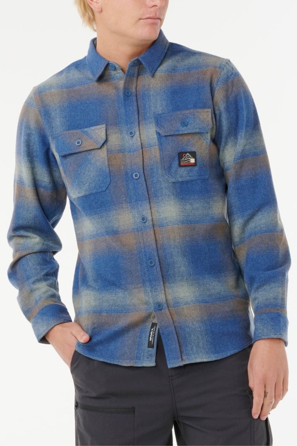 Wearing the Rip Curl Search Wool Flannel—a blue and brown plaid wool button-up with two chest pockets, one with a patch—and dark pants, this look is perfect for relaxed coastal living.