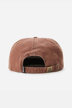 The brown, weathered Rip Curl Searchers Canvas Cap is shown from the back, featuring an adjustable strap with a brass buckle. A small tag is on the left side and a subtle embroidered logo graces the buckle. It rests against a plain, light gray background.