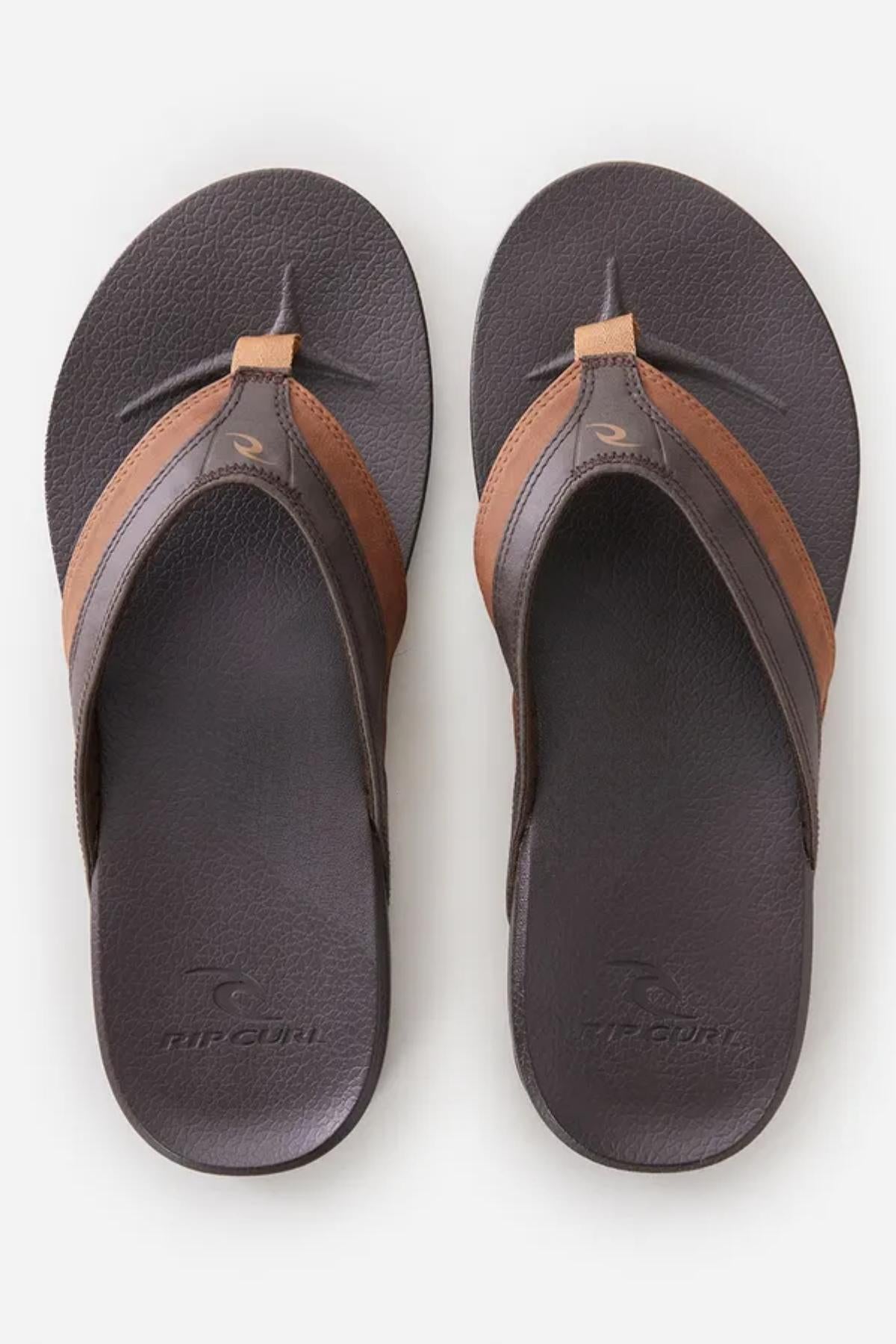 A pair of Rip Curl Soft Top Thongs in brown and dark brown resting on a plain white background. The thongs feature toe post straps with a brown stripe on each side and the Rip Curl logo embossed on the footbed.